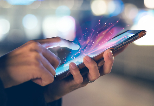 Primer plano de alguien usando un teléfono móvil. La pantalla del teléfono emite rayos de luz.